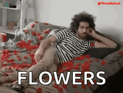 Man In Striped Shirt Laying On Rose Petals With Word Flowers GIF