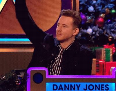 Man In Striped Shirt Standing Before Danny Jones Sign GIF