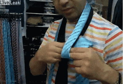 Man In Striped Shirt Tying Blue Tie In Front Of Liveleak Sign GIF