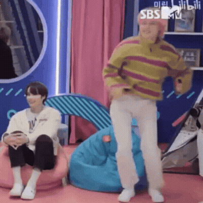 Man In Striped Sweater Dancing Next To Man On Bean Bag Chair GIF