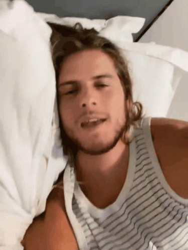Man In Striped Tank Top Laying On White Sheets GIF