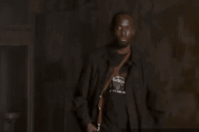 Man In Suit And Bow Tie Holding Gun In Dark Room GIF