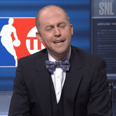 Man In Suit And Bow Tie Sitting In Front Of SNL Sign GIF