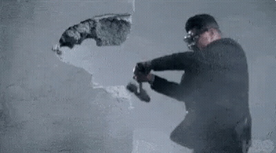 Man In Suit And Goggles Breaking Wall With Hammer GIF
