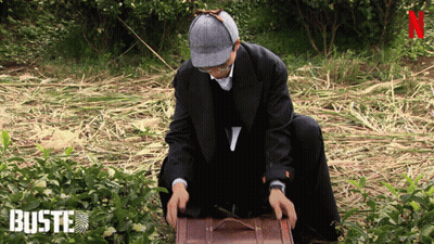 Man In Suit And Hat Kneeling With Suitcase In Front Of Buste Sign GIF