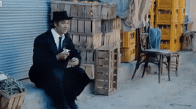 Man In Suit And Hat Sitting On Ledge Eating GIF