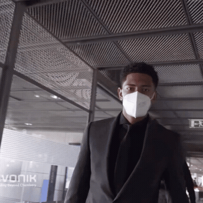 Man In Suit And Mask Walking Past Vonik Sign GIF