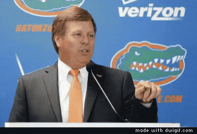 Man In Suit And Orange Tie At Podium With Verizon Logo GIF