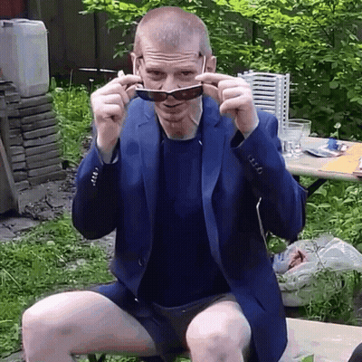 Man In Suit And Shorts Adjusting Sunglasses On Bench GIF