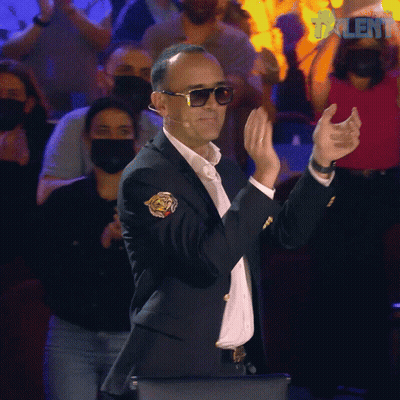 Man In Suit And Sunglasses Applauding In Front Of Masked Crowd GIF