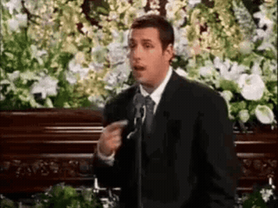 Man In Suit And Tie At Microphone In Front Of Coffin GIF