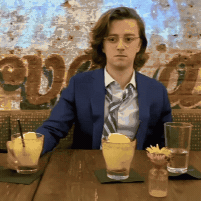 Man In Suit And Tie At Table With Drinks And Avocado Sign GIF