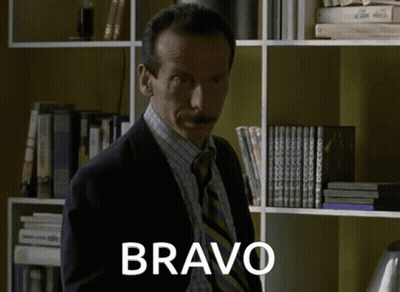 Man In Suit And Tie By Bookshelf With Bravo GIF