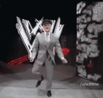 Man In Suit And Tie Dancing In Front Of Wrestling Logo GIF