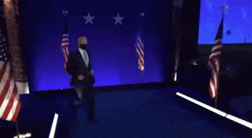 Man In Suit And Tie Dancing On Stage With American Flags GIF