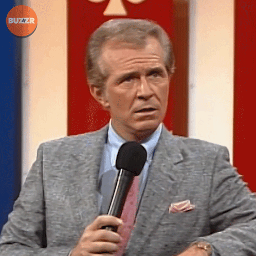 Man In Suit And Tie Holding Microphone In Front Of Buzzr Button GIF