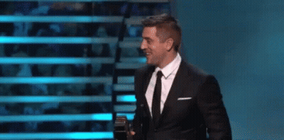 Man In Suit And Tie Holding Microphone On Stage GIF