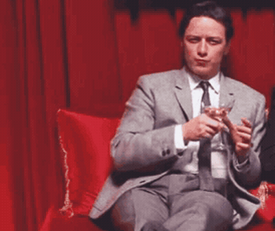 Man In Suit And Tie Holding Wine Glass On Red Couch GIF