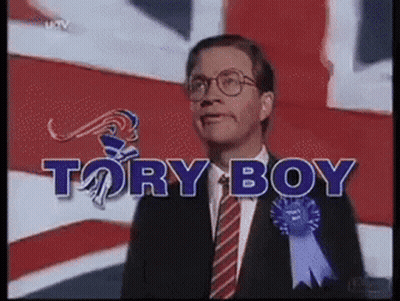 Man In Suit And Tie In Front Of Tory Boy Sign GIF