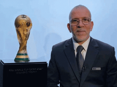 Man In Suit And Tie Next To FIFA World Cup Qatar 2022 Winner's Trophy GIF