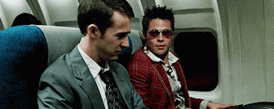 Man In Suit And Tie Next To Man In Sunglasses On Plane GIF