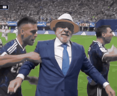Man In Suit And Tie On Soccer Field Surrounded By Players GIF