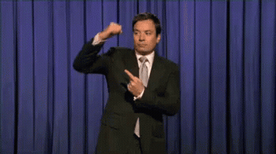 Man In Suit And Tie On Stage With Blue Curtain GIF