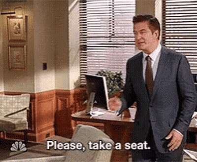 Man In Suit And Tie Saying Please Take A Seat GIF