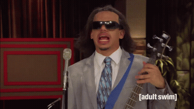 Man In Suit And Tie Singing Into Microphone Holding Adult Swim Guitar GIF