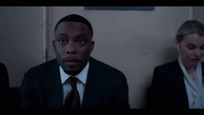 Man In Suit And Tie Sits Next To Woman In Suit GIF