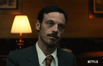 Man In Suit And Tie Sitting At Netflix Sign GIF