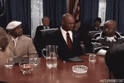Man In Suit And Tie Sitting At Table In Front Of Crowd GIF