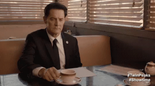 Man In Suit And Tie Sitting At Table With Coffee And Saucer GIF