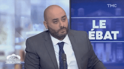 Man In Suit And Tie Sitting In Front Of TMC Screen GIF