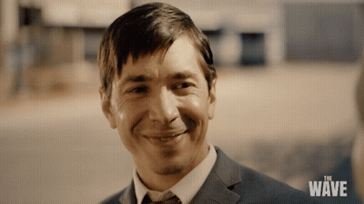Man In Suit And Tie Smiling At The Wave Sign GIF
