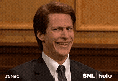Man In Suit And Tie Smiling Beside SNL Hulu Sign GIF