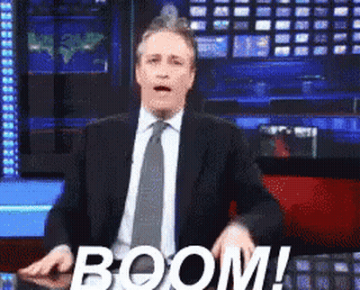 Man In Suit And Tie Standing Beside Boom Sign GIF