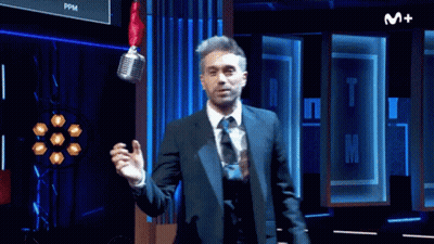 Man In Suit And Tie Standing In Front Of M+ Sign GIF