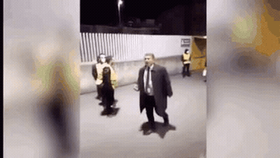 Man In Suit And Tie Walking Down Street Next To Fence GIF