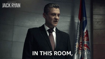 Man In Suit And Tie With Flag Saying In This Room GIF