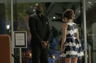 Man In Suit And Woman In Dress In Front Of Erica Lopez Sign GIF