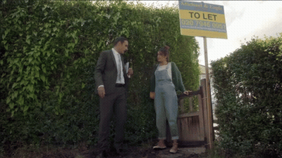 Man In Suit And Woman In Overalls Next To To Let Sign GIF