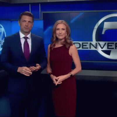 Man In Suit And Woman In Red Dress In Front Of Denver Sign GIF