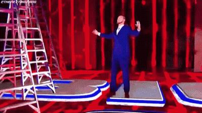Man In Suit Arms Outstretched On Red Stage GIF