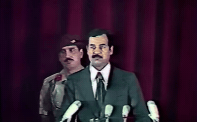 Man In Suit At Microphones With Military Behind GIF