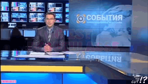 Man In Suit At News Desk With Cobbitnia On Screen GIF