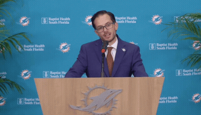 Man In Suit At Podium With Baptist Health South Florida Logos GIF