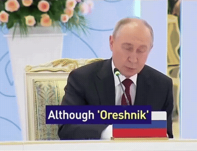 Man In Suit At Table With Sign Although Oreshnik GIF