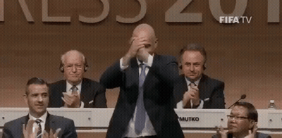 Man In Suit Covering Face While Men Applaud GIF
