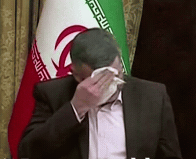 Man In Suit Covering Face With Napkin Near Iranian Flag GIF